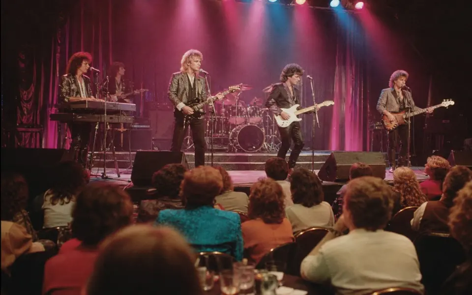 Illustration: a pop-rock band on a mid-size casino theatre stage under magenta and cyan lights